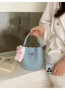 Détail de sac seau texturé bleu clair avec pendentif lapin et serrure en métal.