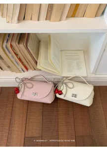 Detail shot of stylish crossbody bag with pearl bow and cherry charm in a retro setting.