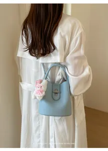 Gros plan du sac seau en cuir bleu clair avec joli pendentif lapin en peluche et fermoir en métal.