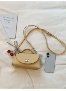 Detail view of yellow minimalist crossbody bag with metal lock, strap, and cherry charm.