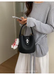 Gros plan détaillé du sac à main sceau en cuir noir avec fermoir tournant en métal et charm duveteux.