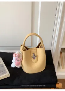 Détail du sac seau jaune en cuir avec pendentif lapin peluche et serrure métallique.