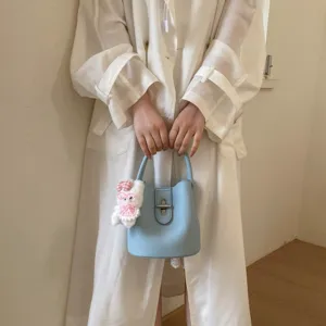 Sac seau en cuir bleu clair pour femmes avec poignée et charm lapin, design élégant.