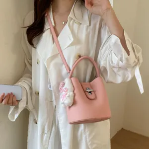 Sac seau en cuir rose pour femme avec fermeture métallique chic et pendentif en peluche.