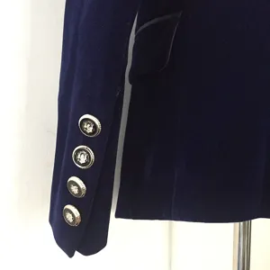 Close-up of women's dark blue velvet blazer sleeve, featuring elegant metallic crest buttons.
