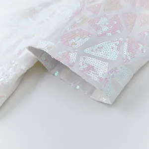 Close-up detail of white men's suit jacket cuff with iridescent pink triangular sequins pattern.