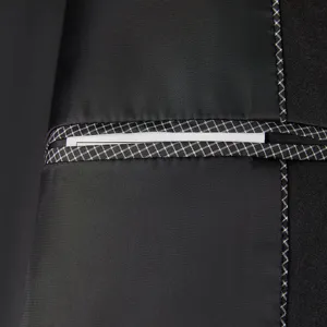 Men's black suit jacket detail view showing elegant grid trimmed pocket and contrast stitching.
