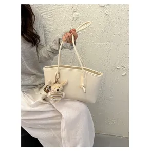 Minimalist beige tote bag for women, stylish shoulder handbag with cute bear charm for daily commute.