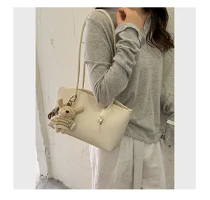 Detail view of elegant beige tote bag shoulder strap and cute knitted bear pendant.