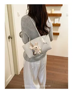 Detail shot of the minimalist white tote bag with a cute knitted rabbit pendant and strap.