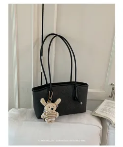 Detail view of a black minimalist tote bag with long handles and a cute bear keychain.