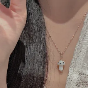 Primer plano de un collar de plata fina con un bonito y pequeño colgante de hongo blanco.