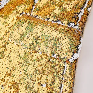 Primer plano detallado de tela de lentejuelas doradas y blancas con textura brillante.
