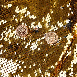 Primer plano detallado de blazer con lentejuelas doradas y botones metálicos de lujo.