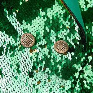 Primer plano de los detalles de una chaqueta de lentejuelas verdes con botones dorados ornamentados.