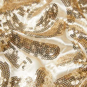 Close-up of gold sequin fabric detail, showing shimmering wave texture and satin surface.