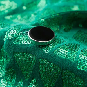 Macro detail of green sequin velvet blazer fabric with geometric triangle patterns and black button.