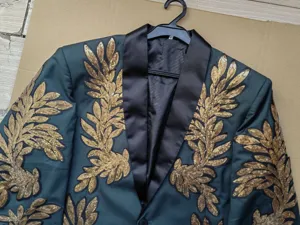 Primer plano de la chaqueta de traje verde oscuro para hombre con bordado de hojas doradas.