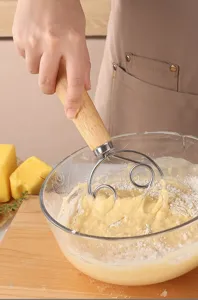 Primer plano de detalle de un batidor de masa de acero inoxidable con mango de madera mezclando.