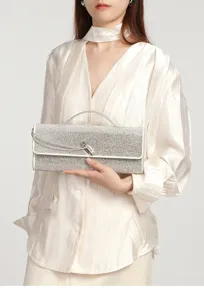 Silver rhinestone evening clutch bag with metal lock detail held by model in detail view.