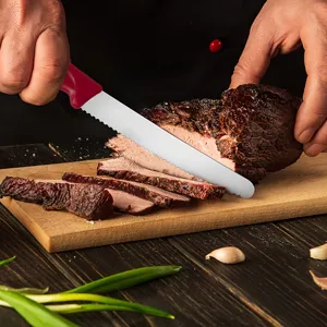 Stainless steel steak knife with red plastic handle slicing roasted meat in detail shot.
