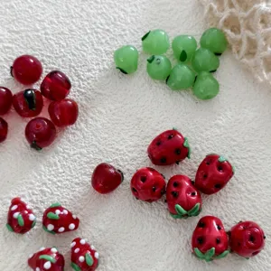Close-up of cute fruit shape glass beads, red strawberry and apple charms for DIY jewelry making.