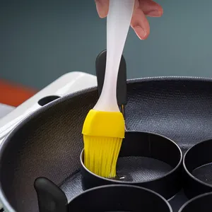 Detailed view of silicone basting brush applying oil on non-stick egg frying pan mold.