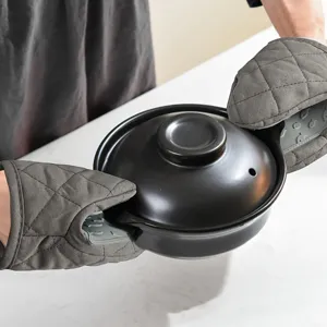 Detail shot showing grey quilted oven mitts with silicone grip, holding pot for heat insulation.