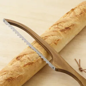 Gros plan sur le couteau à pain en bois coupant une baguette fraîche sur fond en bois.