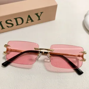 Détail des lunettes de soleil en métal sans monture avec verres roses et griffes dorées.
