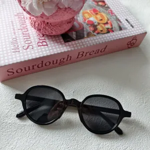 Primer plano de gafas de sol redondas negras en superficie blanca con libro rosa.