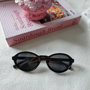 Detailansicht der retro ovalen Sonnenbrille mit schwarzem Gestell und dunklen Gläsern, Accessoire.