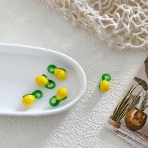 Close-up detail of handmade yellow and green glass fruit charm beads displayed in a white dish.