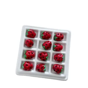 Red glass strawberry beads arranged in a white grid tray for DIY jewelry and hair accessories.