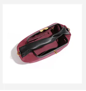 Detailaufnahme der burgunderroten Wildledertasche mit schwarzem Leder und goldenem Verschluss.