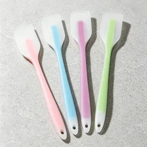 Silicone spatula detail view showing four colorful baking scrapers on textured grey background.