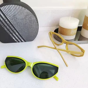 Primer plano detallado de gafas de sol ojo de gato verde neón y amarillo sobre mármol blanco.