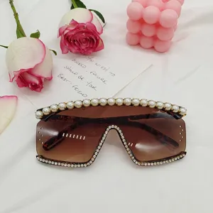 Détail de lunettes de soleil oversize sans monture, verres bruns avec perles et strass.