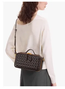 Vue détaillée d'un sac bandoulière en cuir tressé marron foncé porté par un mannequin, mini style.
