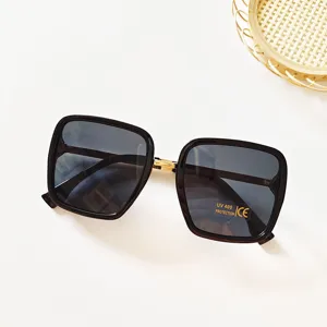 Close-up detail of women square sunglasses featuring dark gradient lenses and gold hinge accent.