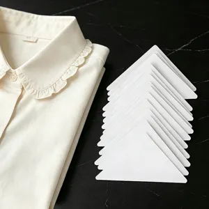 Primo piano di stecche per colletto triangolari bianche per camicie, pila ordinata su marmo.