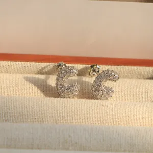 Close-up detail of silver-toned letter stud earrings sparkling with full cubic zirconia stones.