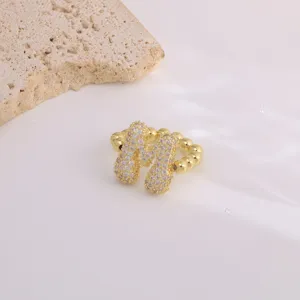 Close-up of gold pavé zircon letter ring with beaded band design on neutral stone prop.