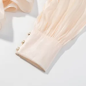 Detailopname van elegante champagnekleurige jurkmand met fijne plooien en parels.