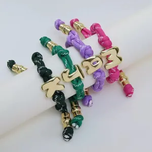 Detailed closeup of colorful woven rope bracelets featuring gold 3D letter charms.