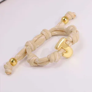 Exquisites Armband aus beige gewebtem Seil mit poliertem goldenen Buchstabe T Anhänger.