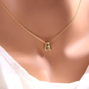 Gros plan détaillé d'un collier pendentif lettre A minimaliste en or sur chaîne fine.