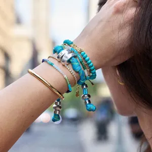 Detail shot of stacked fashion bracelets, featuring blue beads and chic metallic charms.