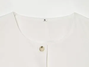 Detailaufnahme des Halsausschnitts einer einfarbigen weißen Leinenweste mit Knopf und Etikett.