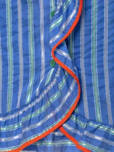 Blue striped sleeveless shirt detail featuring vibrant orange ruffles and green buttons.